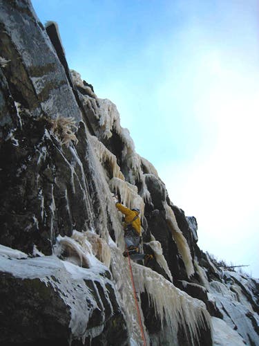 "Freddie Wilkinson leads the crux second pitch of Firing Line (NEI5+ M6) at Cannon Cliff. Photo by Peter Doucette."