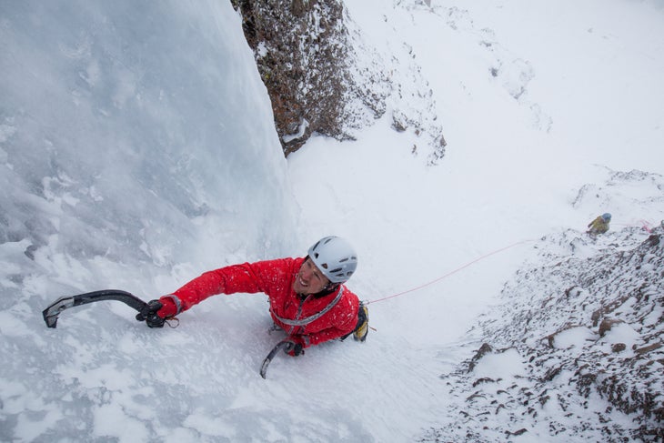 Ice climber climbs waterfall while wearing a helmet.