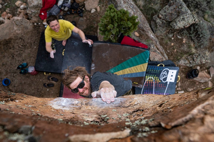 a spotter prepares to catch a climber cruxing out on a boulder problem