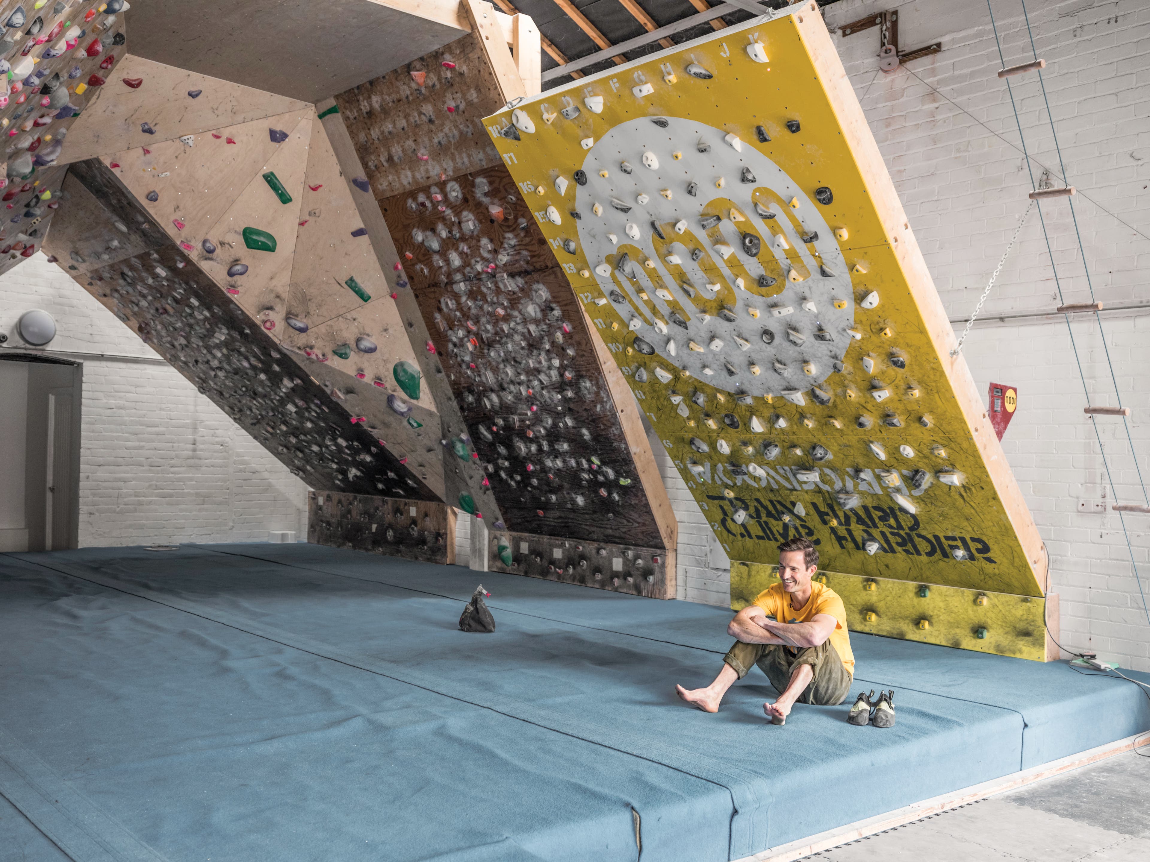 Ben Moon sitting below a MoonBoard in the school room. The famous 50 degree wall is in the background.