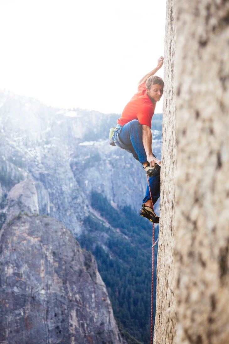 Action_Tommy climbing_(c)BrettLowell_DawnWall Tommy Caldwell climbing The Dawn Wall in a red shirt and pants. His left hand is crimping and he is matching his right foot to his right two fingers.