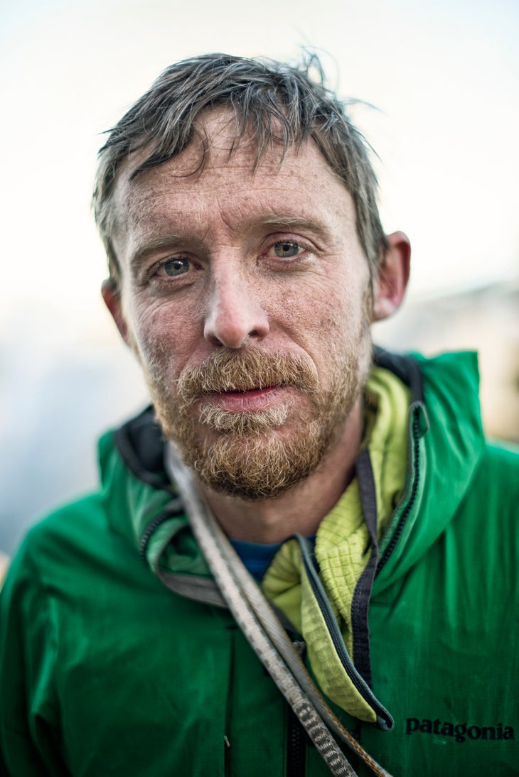 portrait_Tommy Caldwell_(c)BlighGillies Tommy Caldwell looks into camera with a serious face while wearing a green jacket and midlayer - rope slung across his body from shoulder to waist.