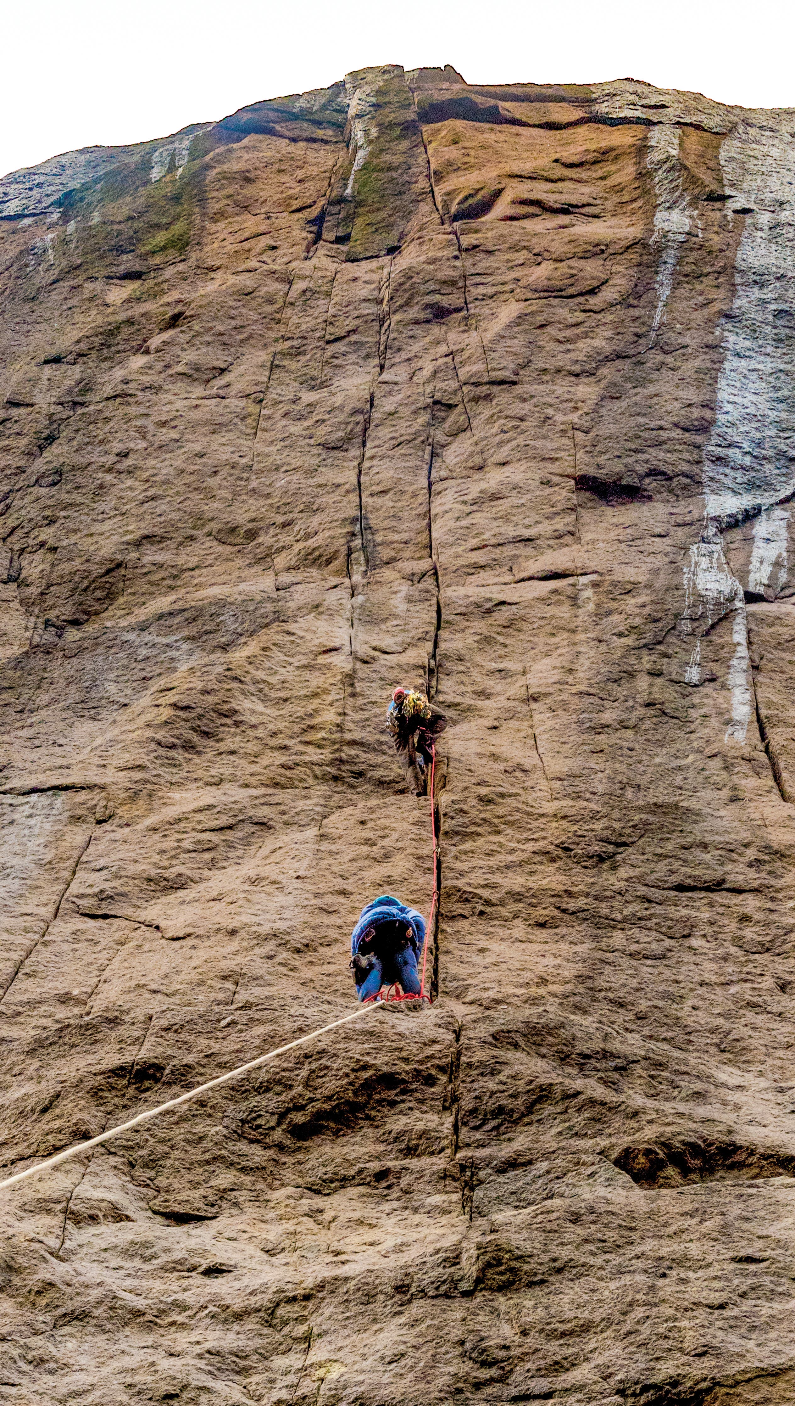 TristanHobson_6302_gn-web Man waiting on a ledge while another climbs a steep cliff face