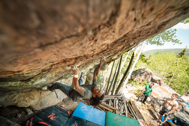 miki Mickael Mawem grits his teeth as he moves up an overhanging boulder section. His teammates look on.