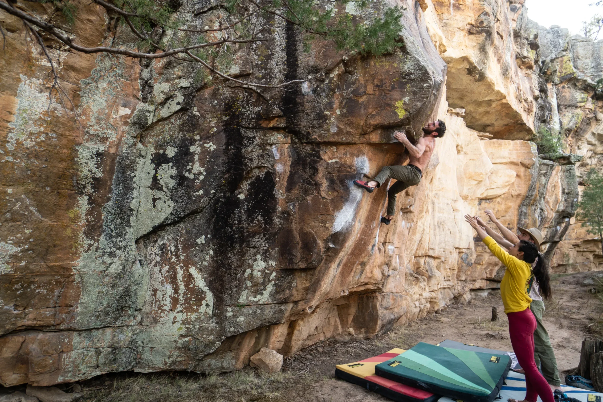 Boulderer climbs above a group of spotters protected by a crash pad.