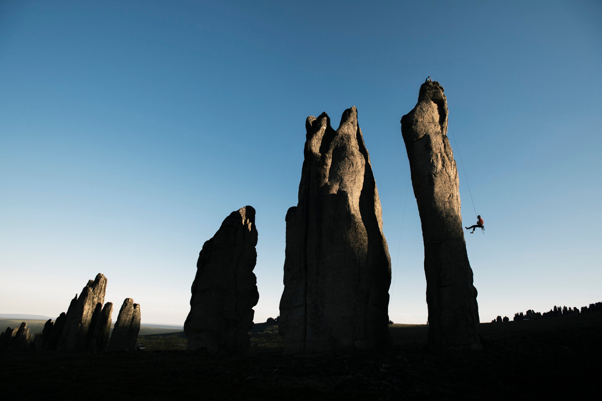 Climber rappels off rock spire at sunset.