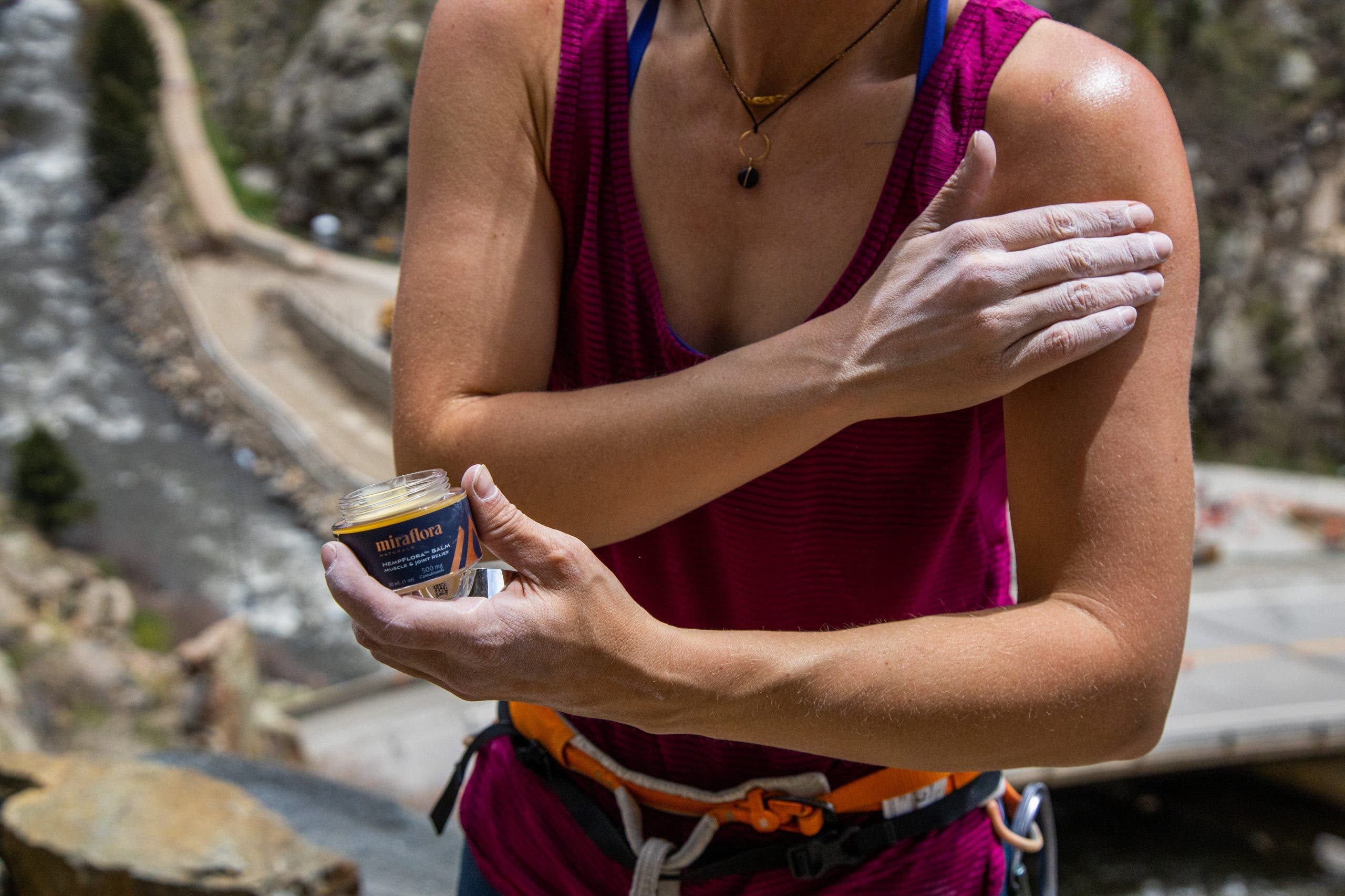 Chelsea Rude promotes climbing recovery by applying Miraflora CBD balm on her shoulder with chalky hands.