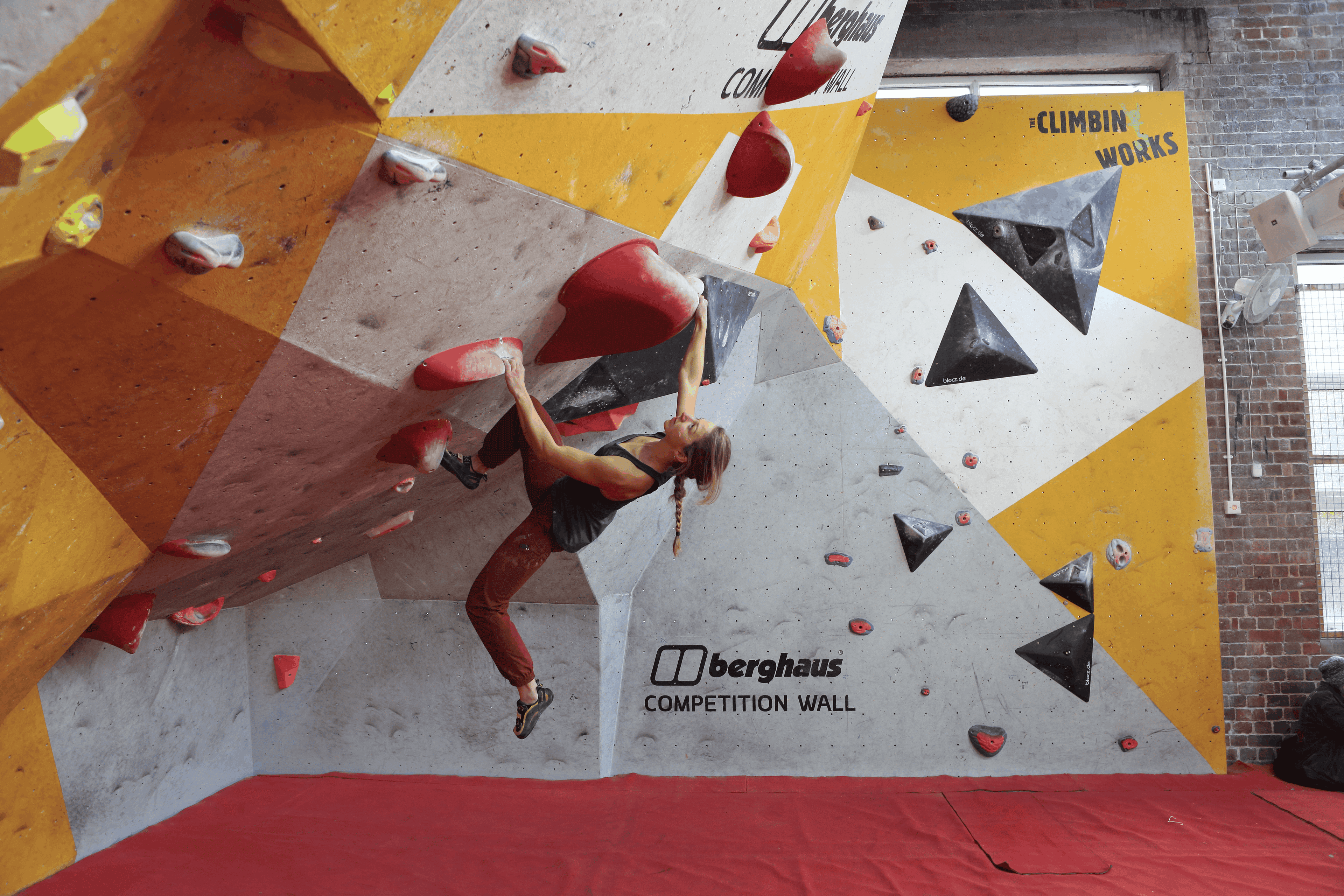 A female climber boulders in a red and yellow gym. climbing training