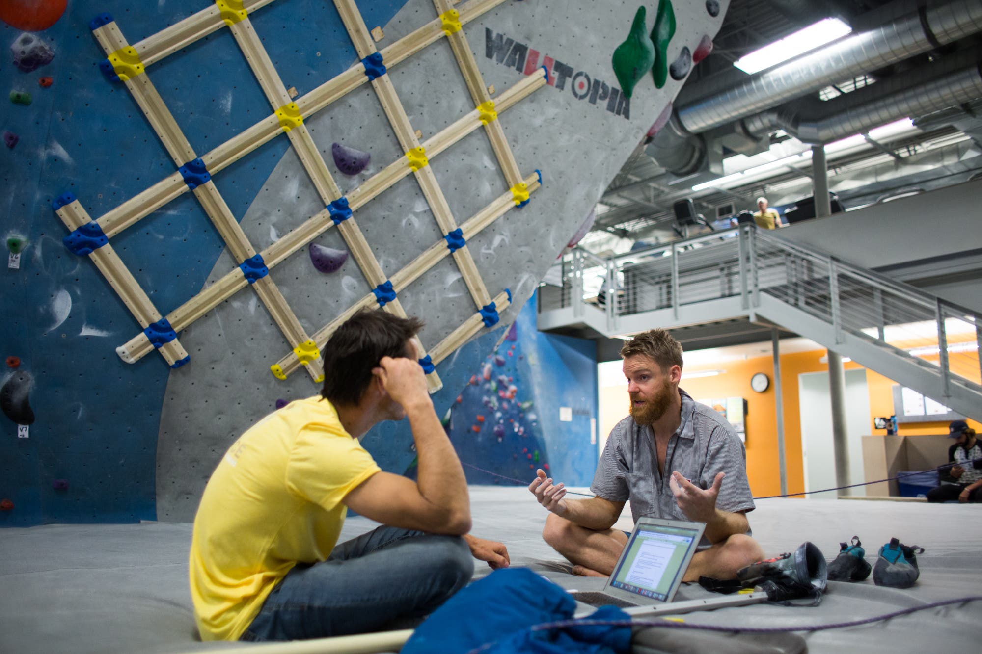 two men sit on a mat under the boulder wall while making a climbing training plan