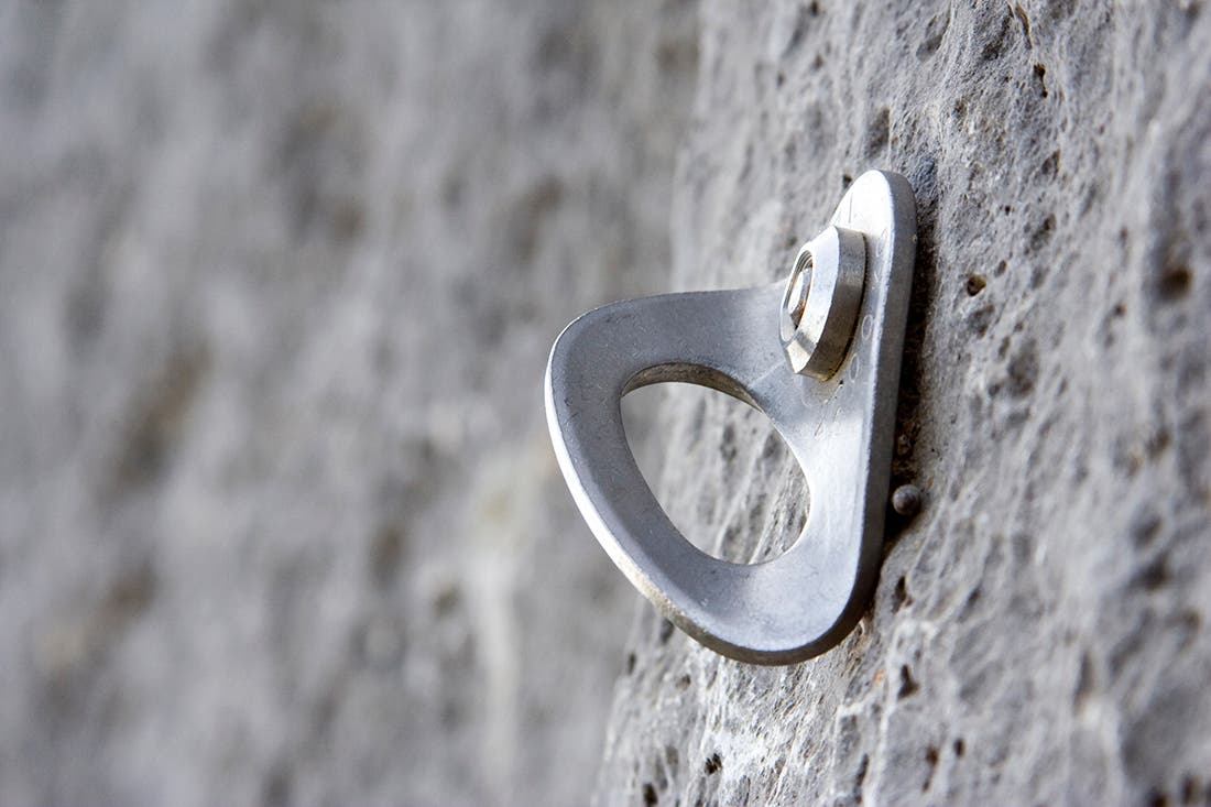 A bolt and hanger fixed to a rocky cliff.