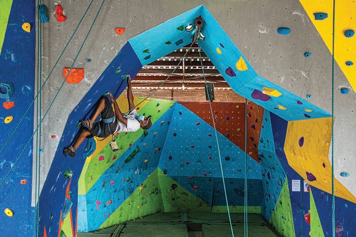 A man climbing a colorful, overhanging, indoor climbing wall in East Africa.