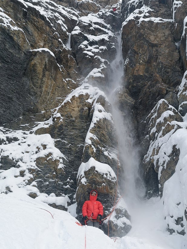 Climbers stands below steep mountain face.