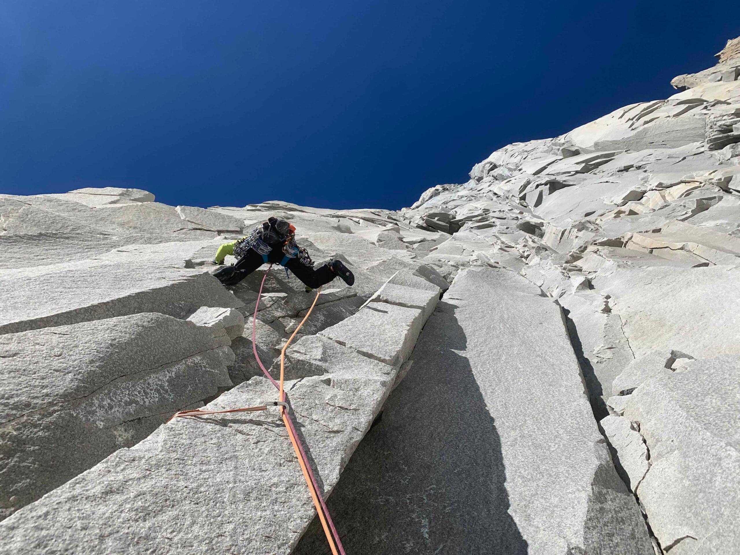 Climber ascends steep, rocky mountain face in Patagonia.