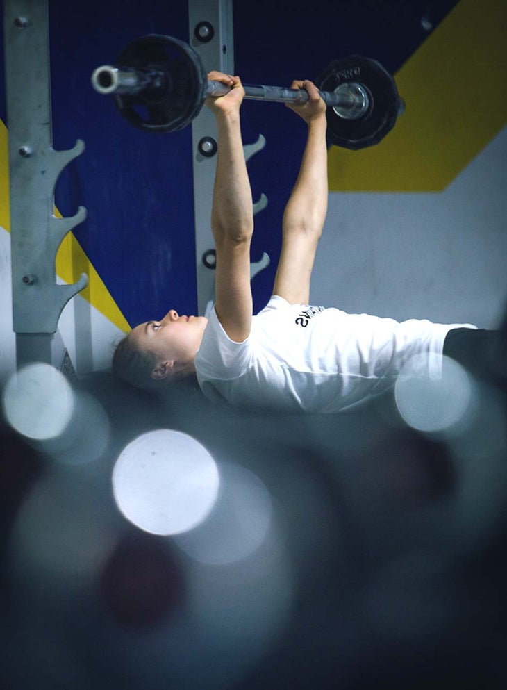Climber Margo Hayes benchpressing weights in a gym.