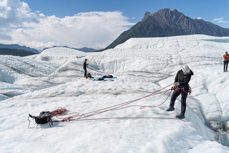 A climbing guide lowers their client into the Root Glacier in June 2022.