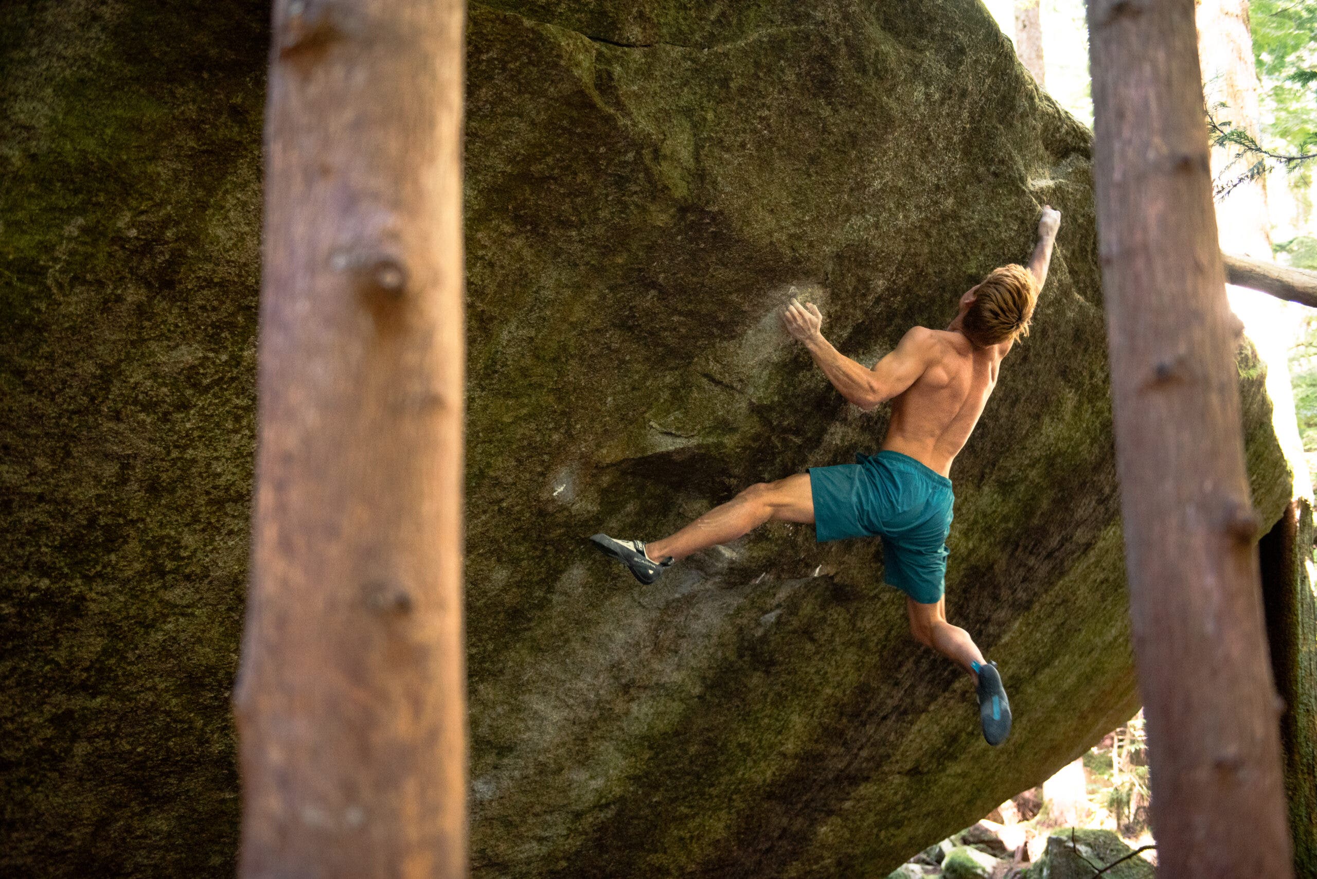 Uchida dynoing high on Shelter, V13, during his flash. He's wearing blue shorts, no shirt. His hair is dyed yellow-gold. His feet are swinging off wildly.