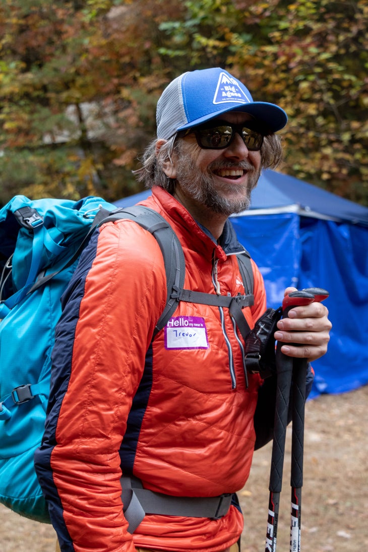 Trevor Hahn, instructor of the visually impaired climbing clinic stands holding his trekking poles at a trailhead in Muir Valley. With sunglasses and a blue hat matching his blue backpack, Trevor wears a smile as wide as the valley floor.