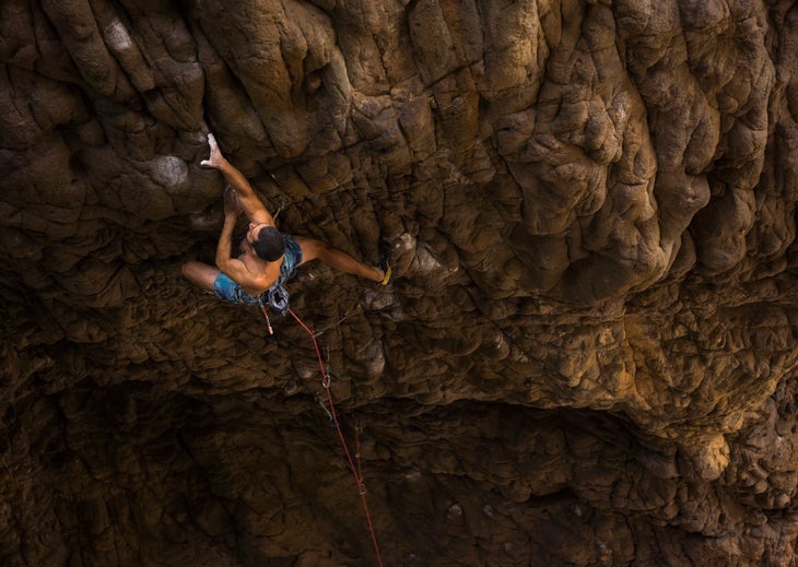A male climber testing his endurance on a steep sport route in Corsica.
