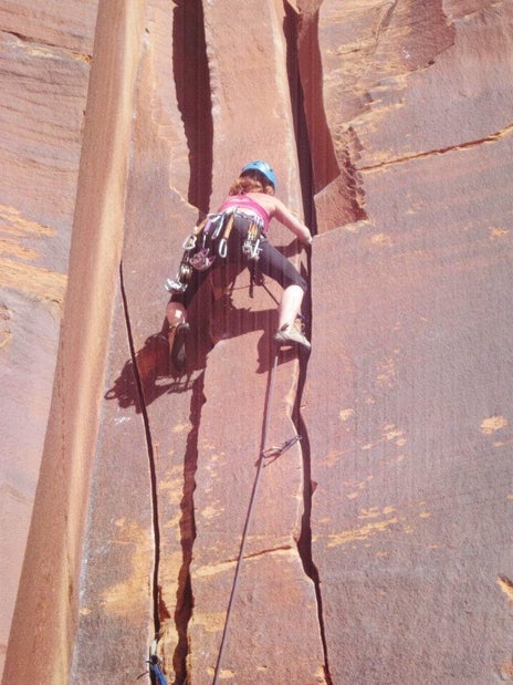 Female rock climber climbs vertical sandstone crack.