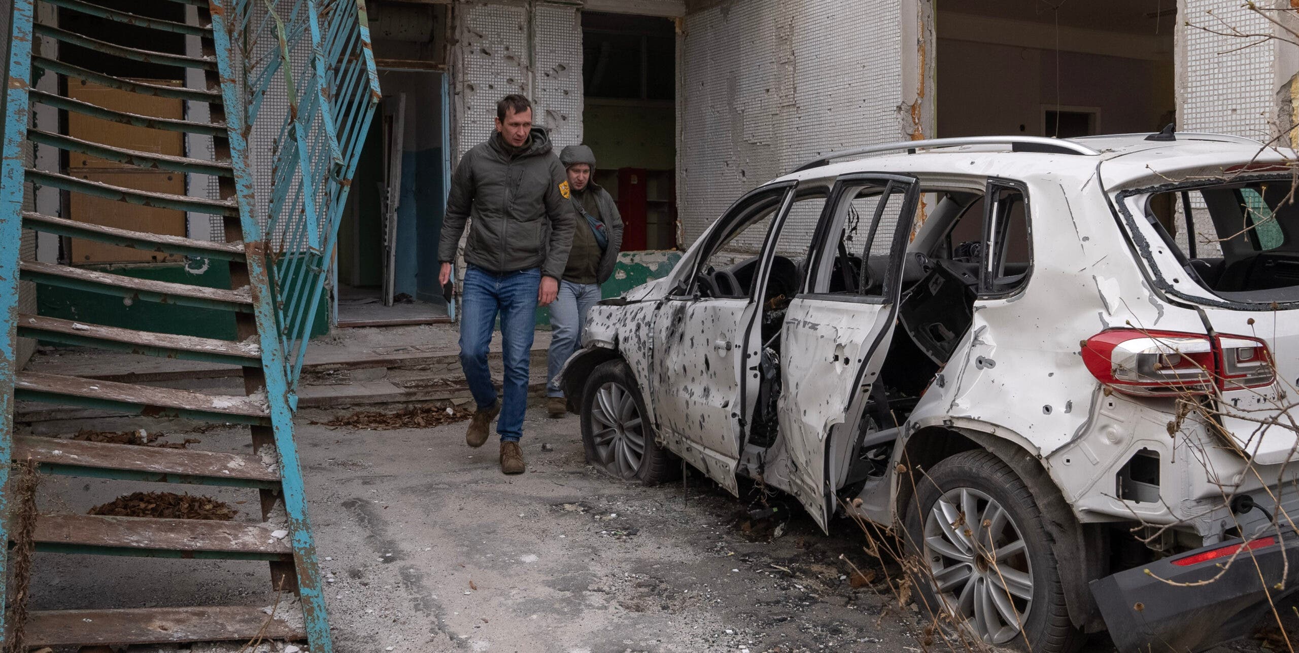 A man walking around a damaged car parked outside a bombed out school in Ukraine