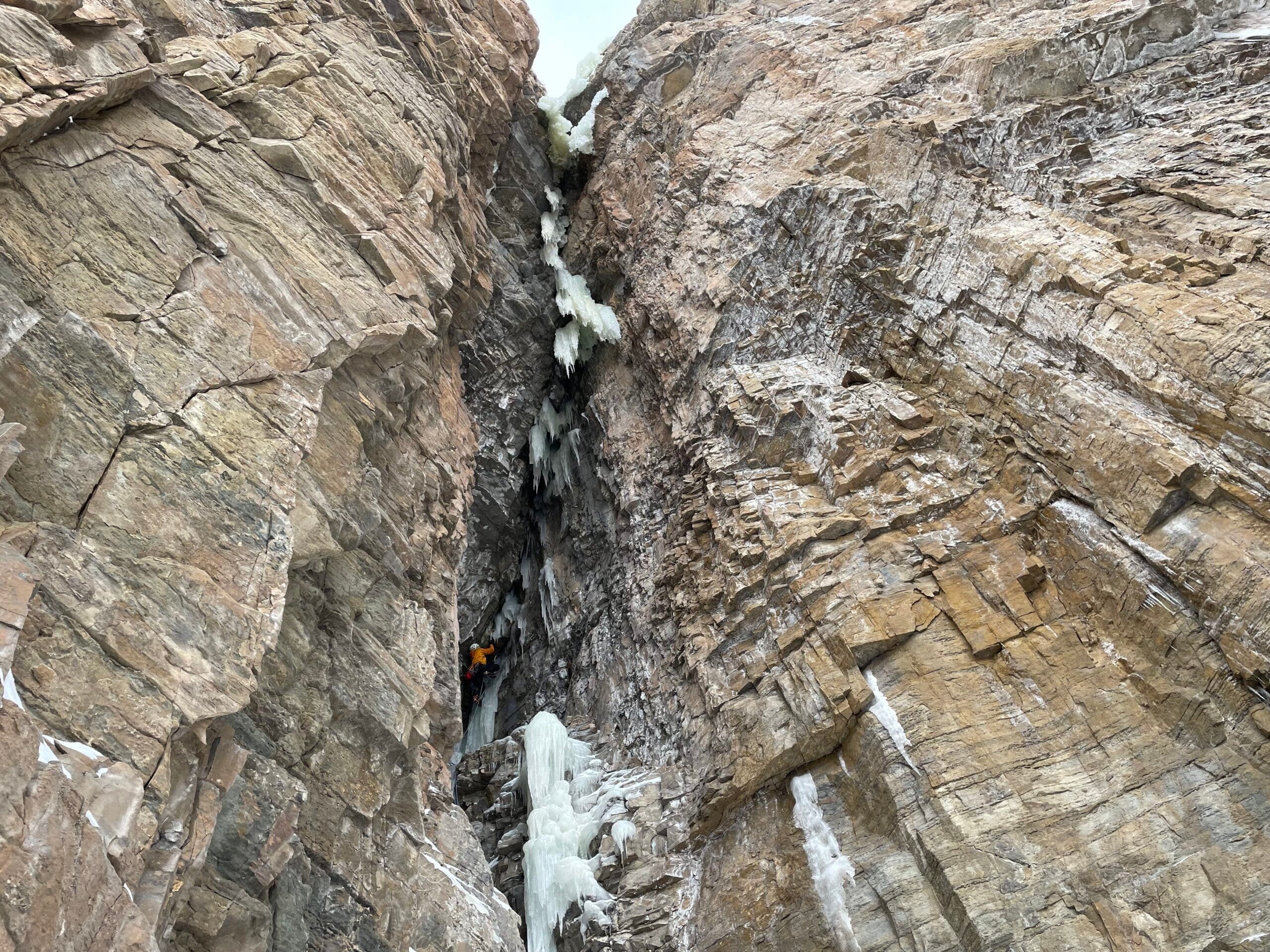 Man climbs a steep rocky chimney filled with ice.
