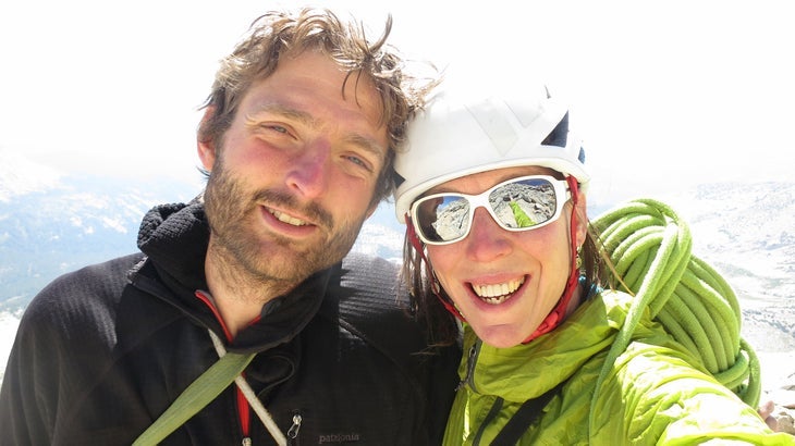 Two rock climbers pose on the summit of a climb, sunny background, no view.