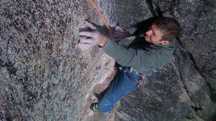 Male in grey sweatshirt climbs a vertical pitch of rock.
