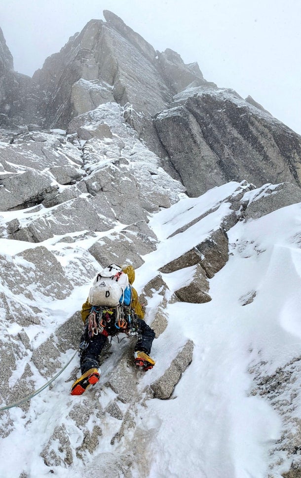 A climber leads up a snowy granite slab.