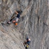 男性攀岩者持有到陡峭的灰色角落而保护者抬起头。