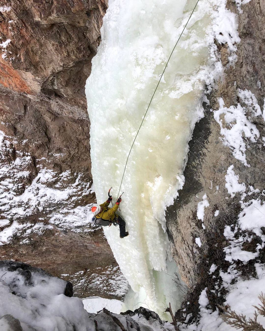 Climber top ropes a steep ice column.