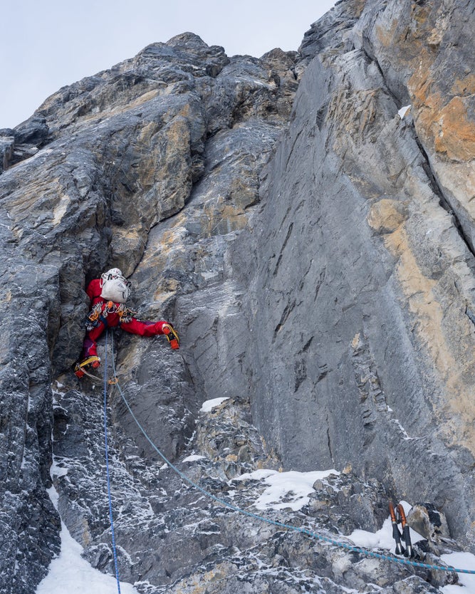 Alpinist in red jacket stems up a rocky corner.