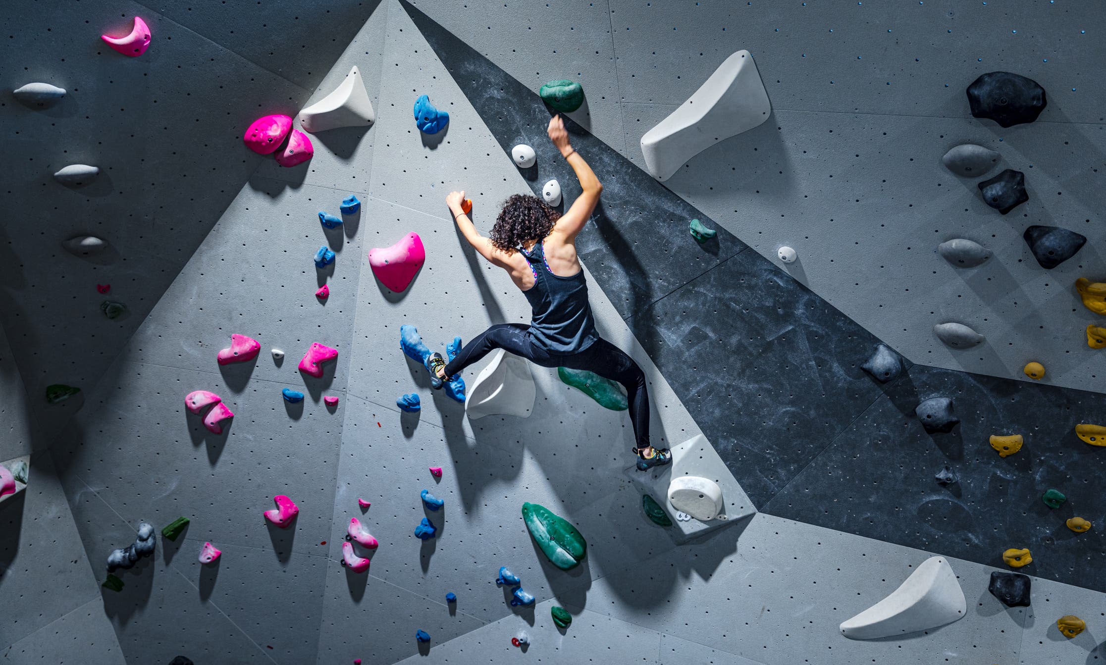 Fit young woman climbing wall in gym.