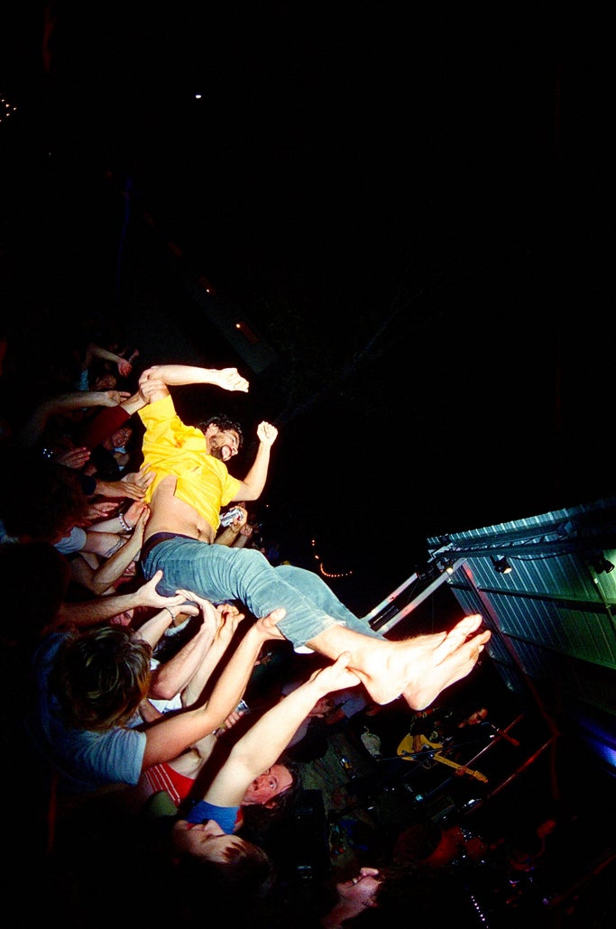 Man in yellow shirt crowd surfs at night