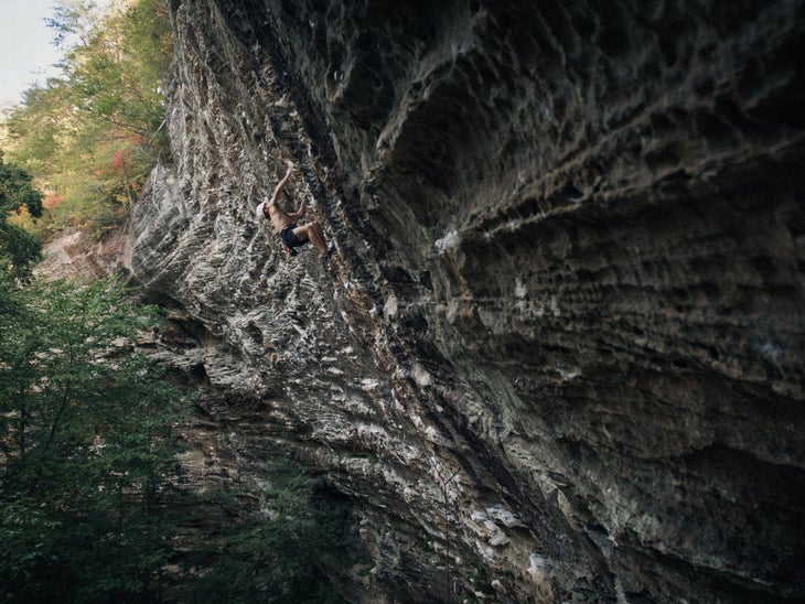 Man in shorts climbs overhanging sandstone cliff in Kentucky.
