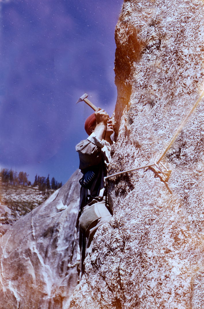 Man hammers in piton on granite face on a sunny day.