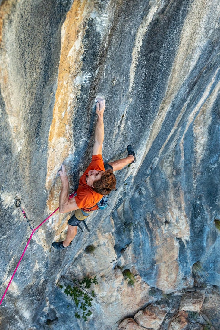 Seb Bouin in an orange shirt sticking one of the crux moves of Lapsus