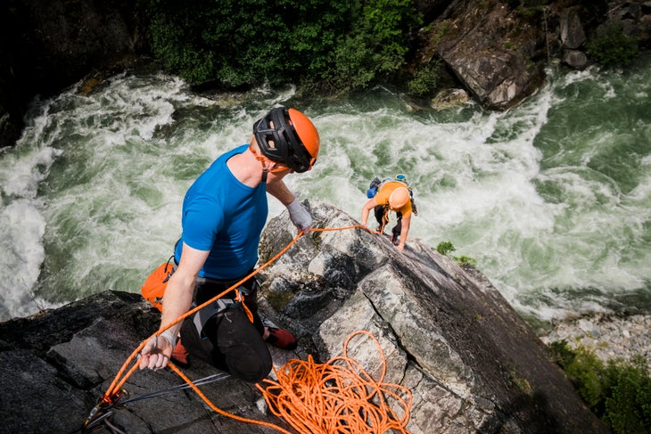 Squamish, BC , CAN - June , 08, 2021: A male rock climber belays his climbing partner up a dramatic rock climb that is named Star Chek near Whistler, British Columbia on June 8th, 2021. Far bellow is the raging Cheakamus River which cuts through this dramatic canyon, halfway between Squamish and Whistler. Due to its picturesque location and relatively easy difficulty Star Chek is considered a top 100 rock climbing the Squamish area.