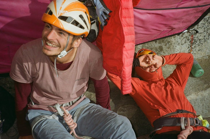 Two climbers on a ledge on El Capitan, wearing helmets, looking happy.