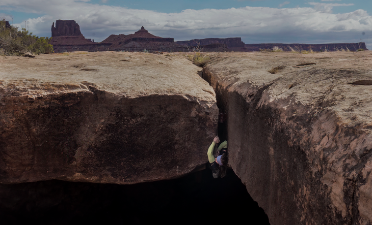 A view of the White Rim with Mary Eden climbing a roof crack in the foreground.