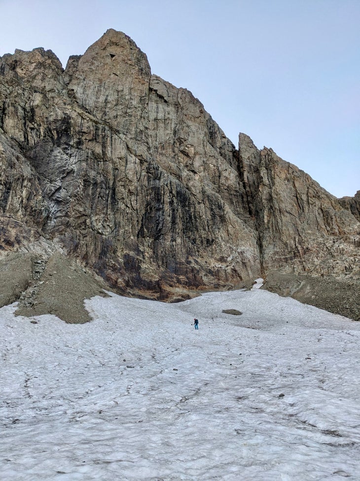 A climber on a glacier beneath a foreboding alpine big wall.