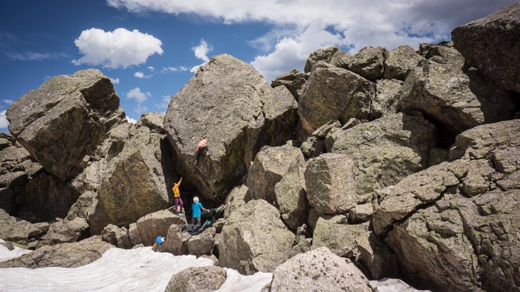 A man climbing a tall boulder problem in Upper Upper Chaos Canyon. The landing is quite bad and his friends have a number of pads angled around trying to make his fall safe.