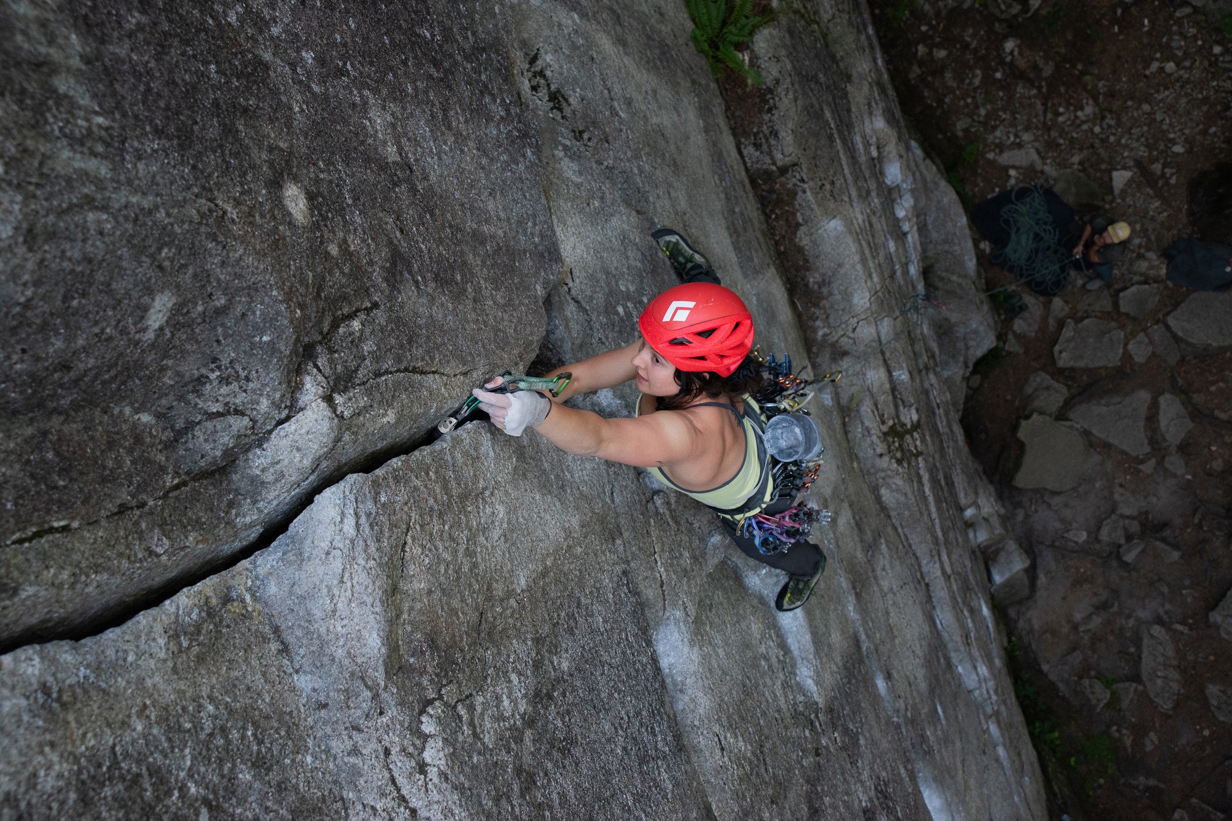 Female climber wearing red helmet placing cam in crack on rock wall.