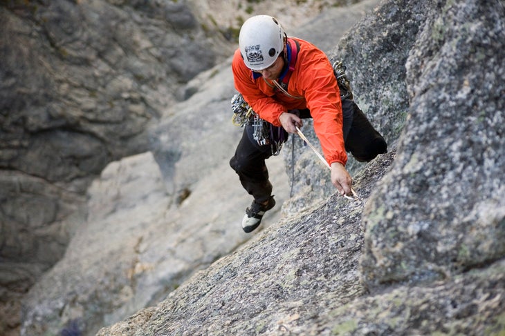 The author in a helmet, rock shoes, and windbreaker aid climbing on a large granite wall in the North Cascades.