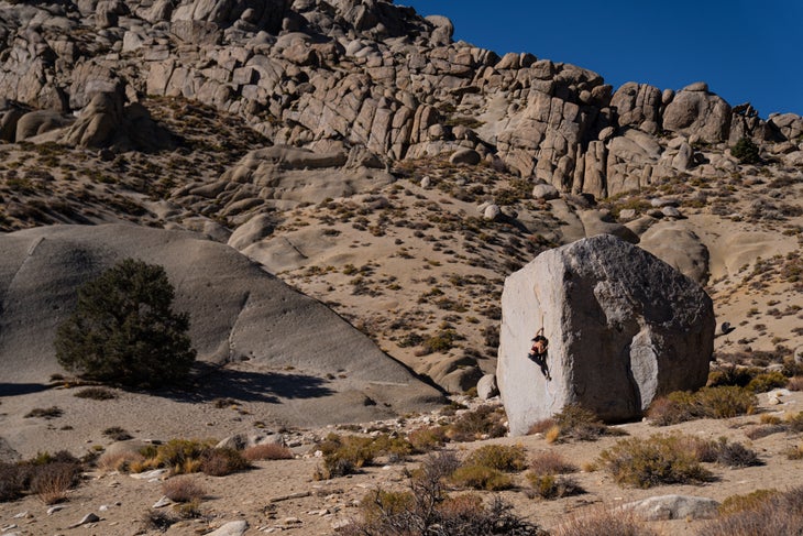 A woman climbing a tall V4 boulder problem in Bishop, CA.