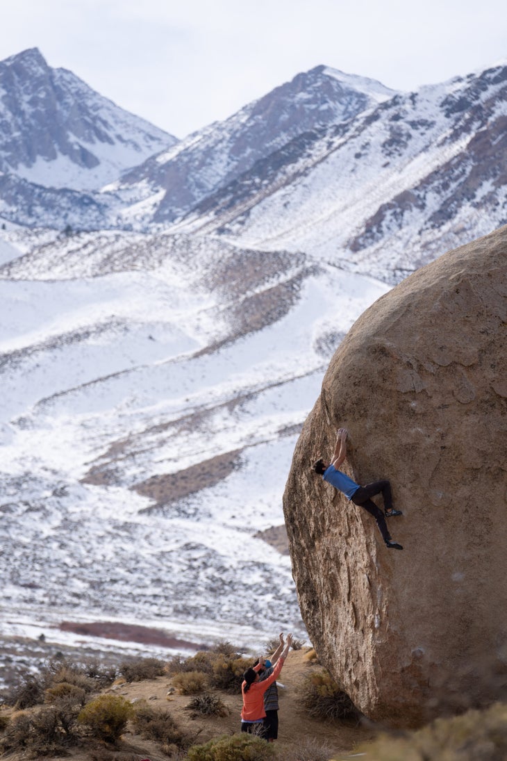 A climber on a tall boulder in Bishop with the lower slopes of Mount Tom in the background.