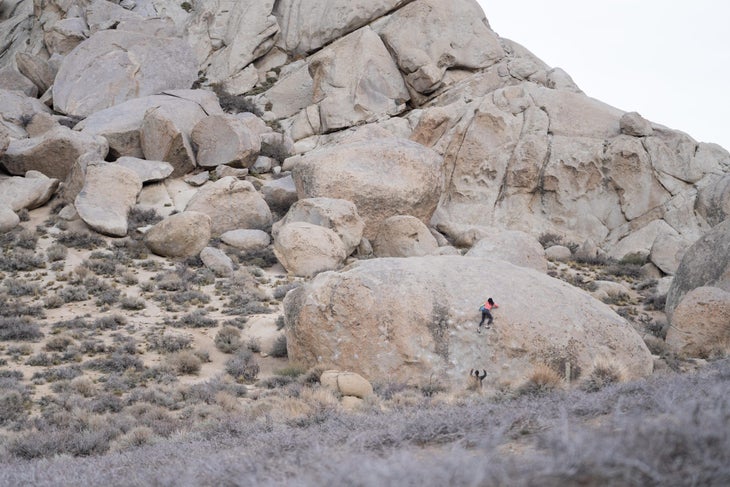 A woman climbing a tall, slabby V2 in Bishop, CA.