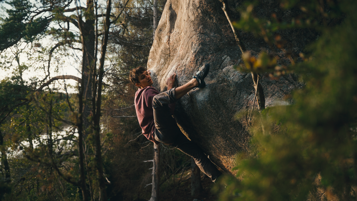 A climber ascending a sloping granite boulder problem in a Finnish foret