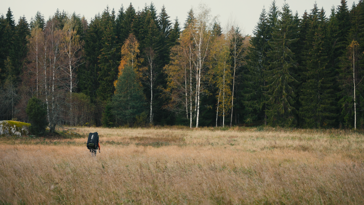 A climber wearing a crashpad walking through an autumnal field in Finland