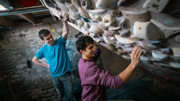 Two professional climbers standing next to a small wooden spray wall in England.