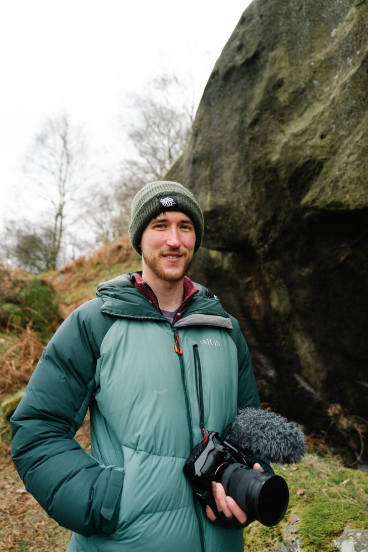 A man, Sam Lawson, holding a camera during a cold day at the boulders.